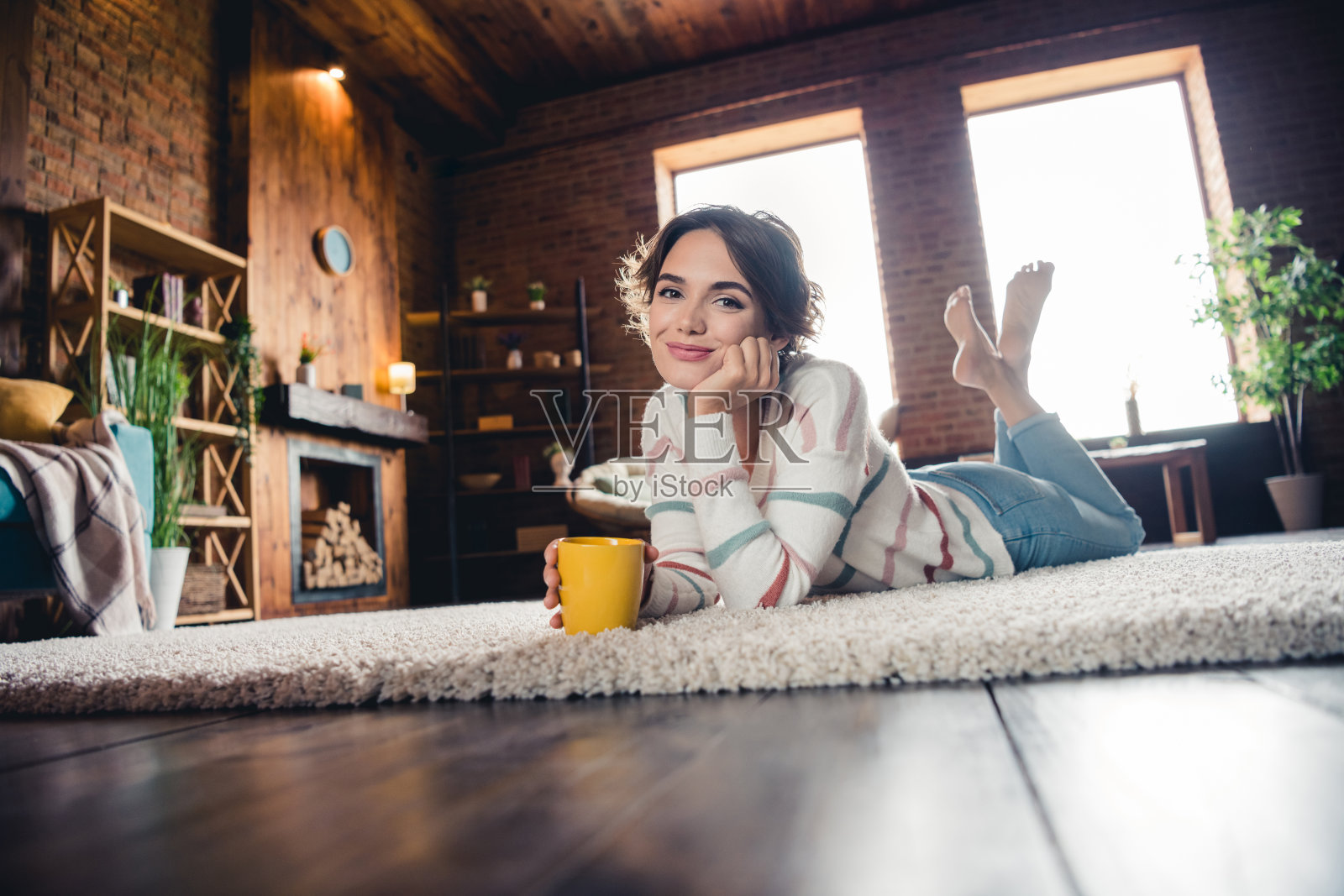 宁静可爱的女孩的全尺寸肖像赤脚躺在地板上，拿着新鲜的香气咖啡杯，在里面度过空闲时间照片摄影图片