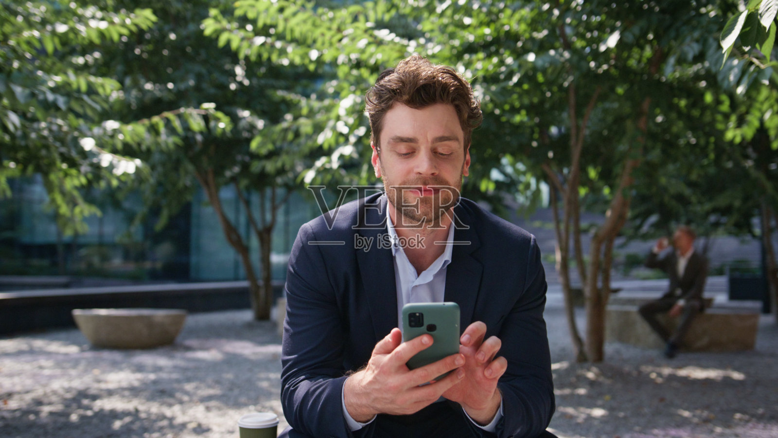 微笑着发短信的商人独自坐在绿广场近距离观看。照片摄影图片
