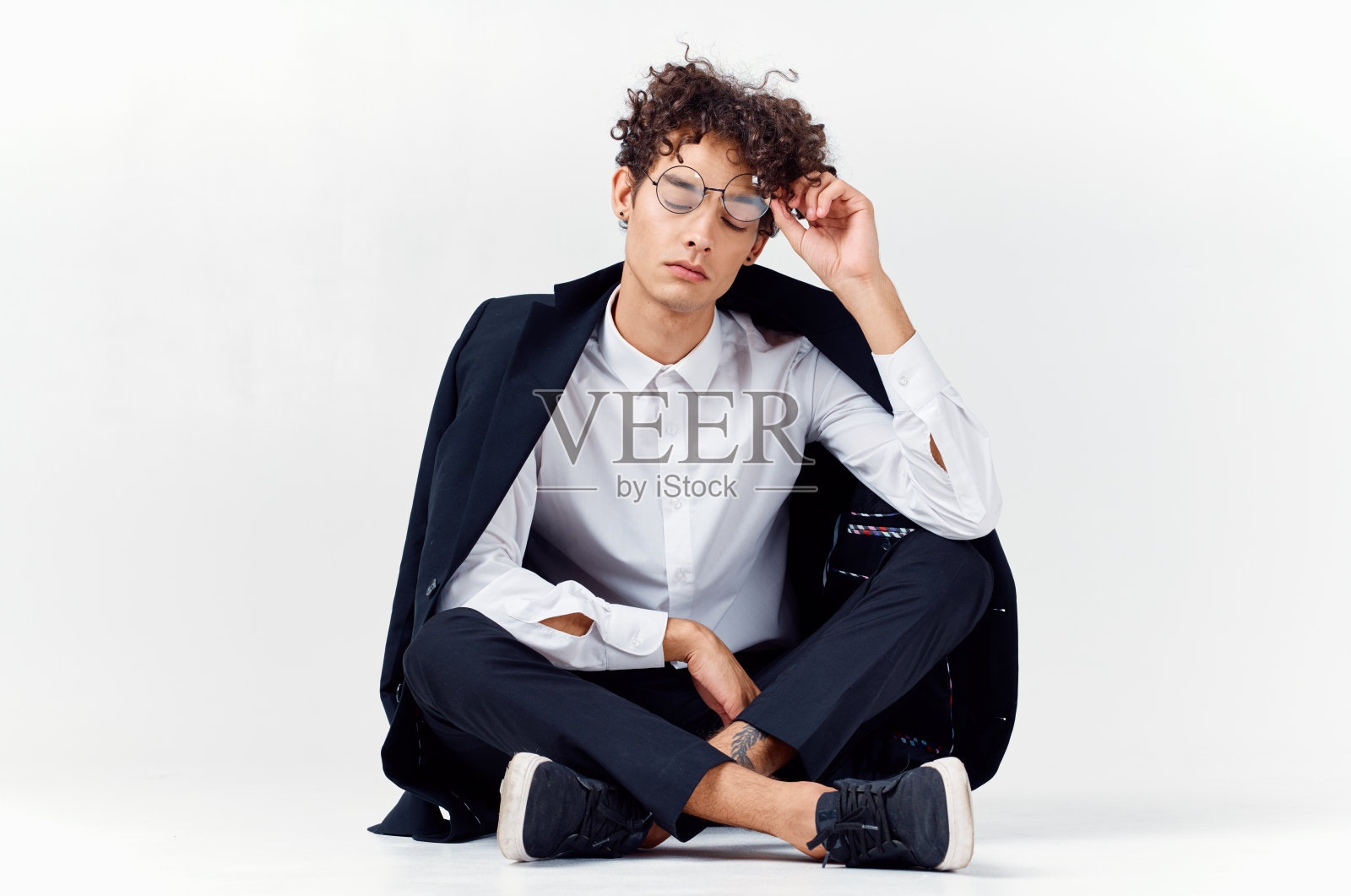 一个穿着长裤、衬衫、夹克和运动鞋的帅哥，在一个明亮的房间里，留着一头卷发照片摄影图片