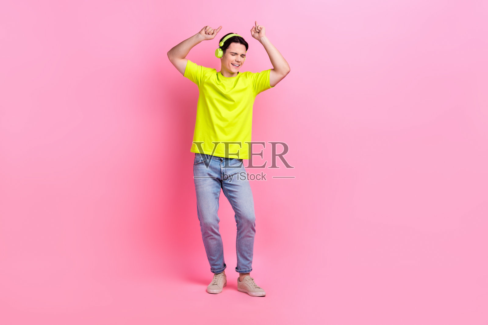 欢快时髦的男人穿着黄色t恤耳机跳舞听音乐孤立的粉红色背景的全长照片照片摄影图片