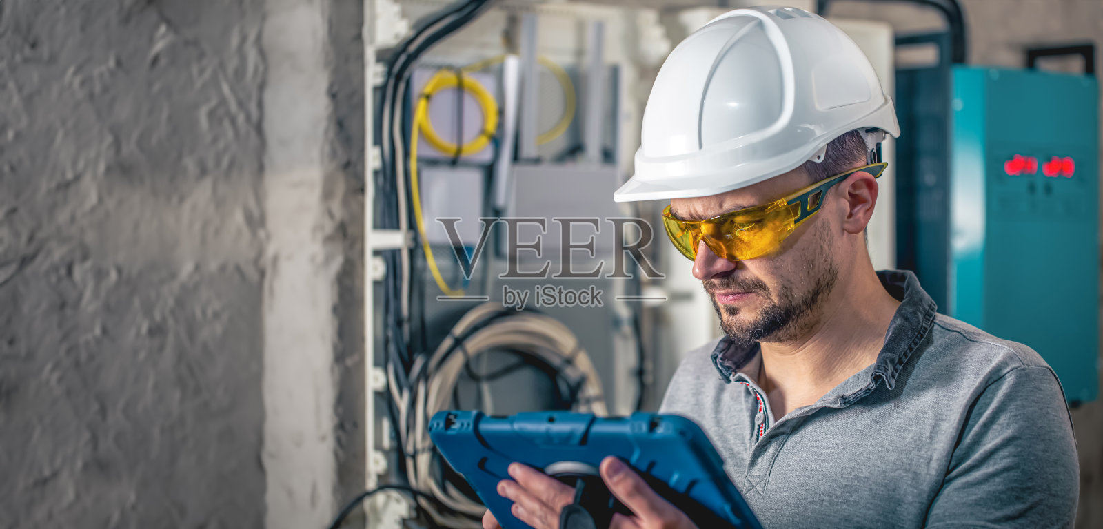 在带保险丝的配电盘工作的电气技术员使用平板电脑。照片摄影图片