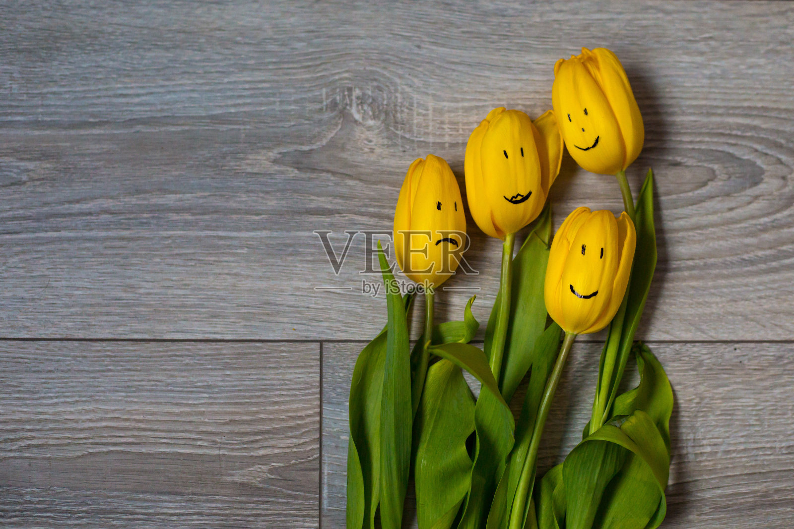 郁金香上画着一张脸。一朵黄色的郁金香躺在木地板上。花上的情感。家庭心理学。花的家族。对花过敏。妇女节。母亲的一天。3月8日。春天。照片摄影图片