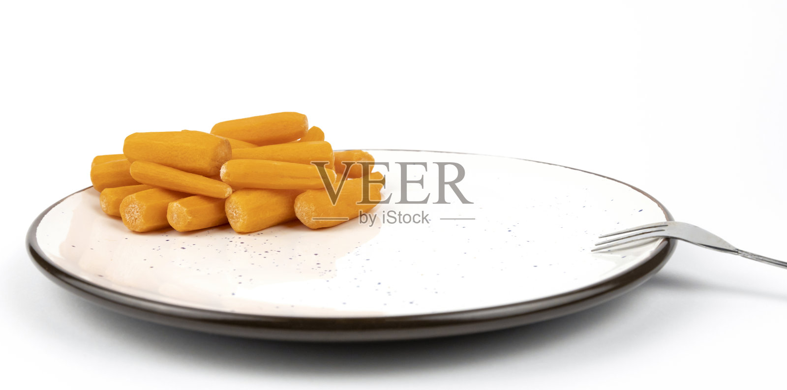 用叉子把小胡萝卜放在盘子里。有机食品的概念。照片摄影图片