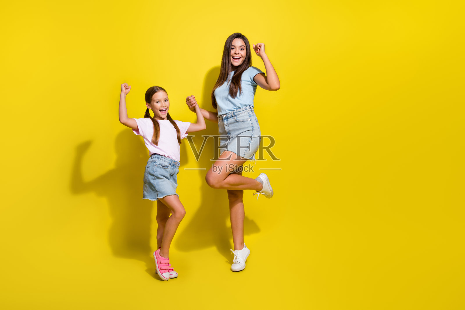 照片中，两个兴奋的女孩在一起度过愉快的周末，在鲜艳的背景下举起拳头照片摄影图片