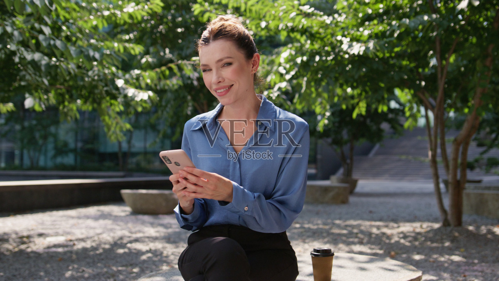 快乐的女孩坐在阳光明媚的街道上，用手机浏览社交媒体。照片摄影图片