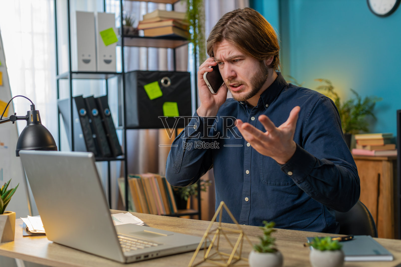 年轻的商人自由职业者接听客户的移动电话，使用智能手机和笔记本电脑照片摄影图片