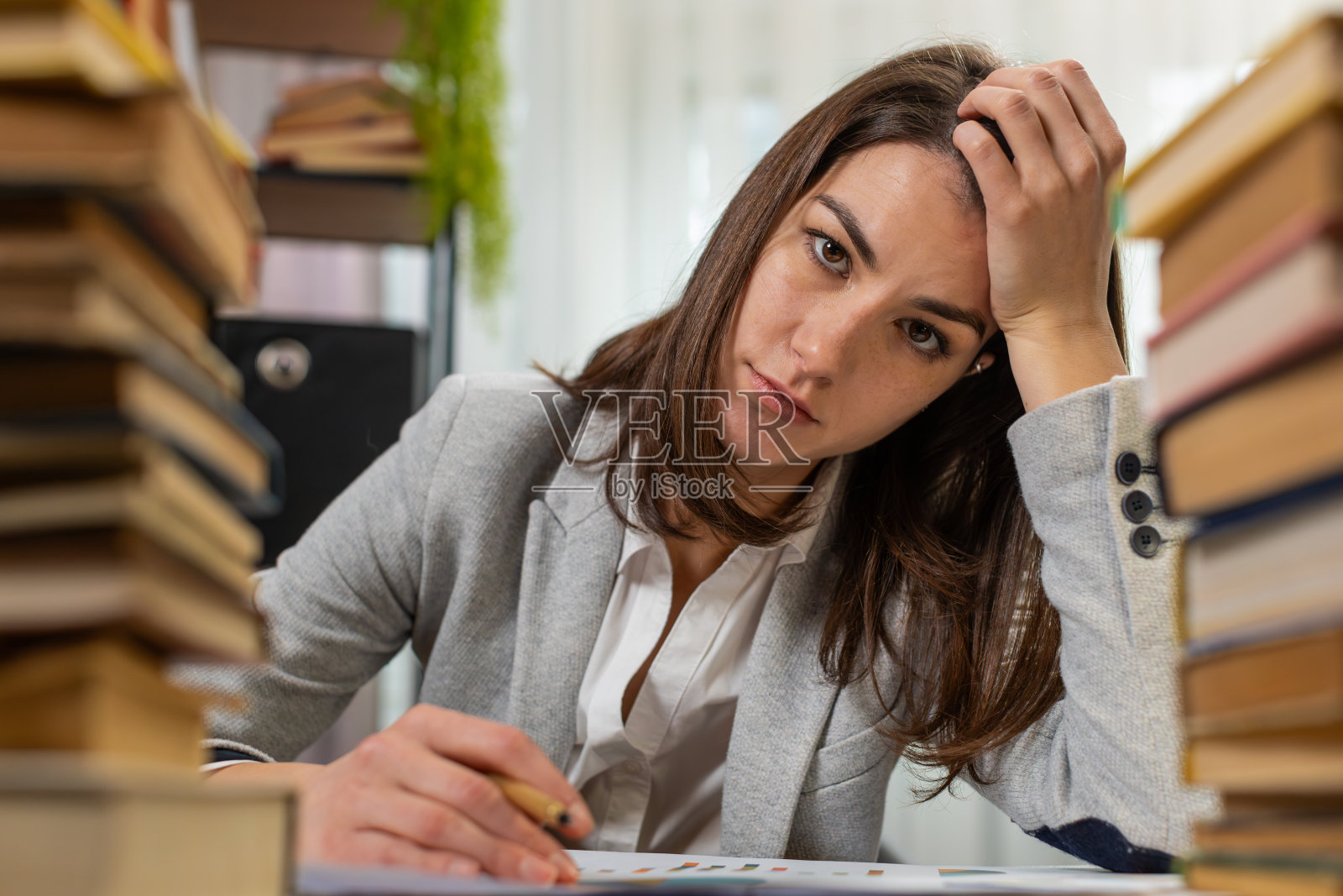 疲惫的女商人看着文件，报告成堆的书，同时在办公室努力工作照片摄影图片