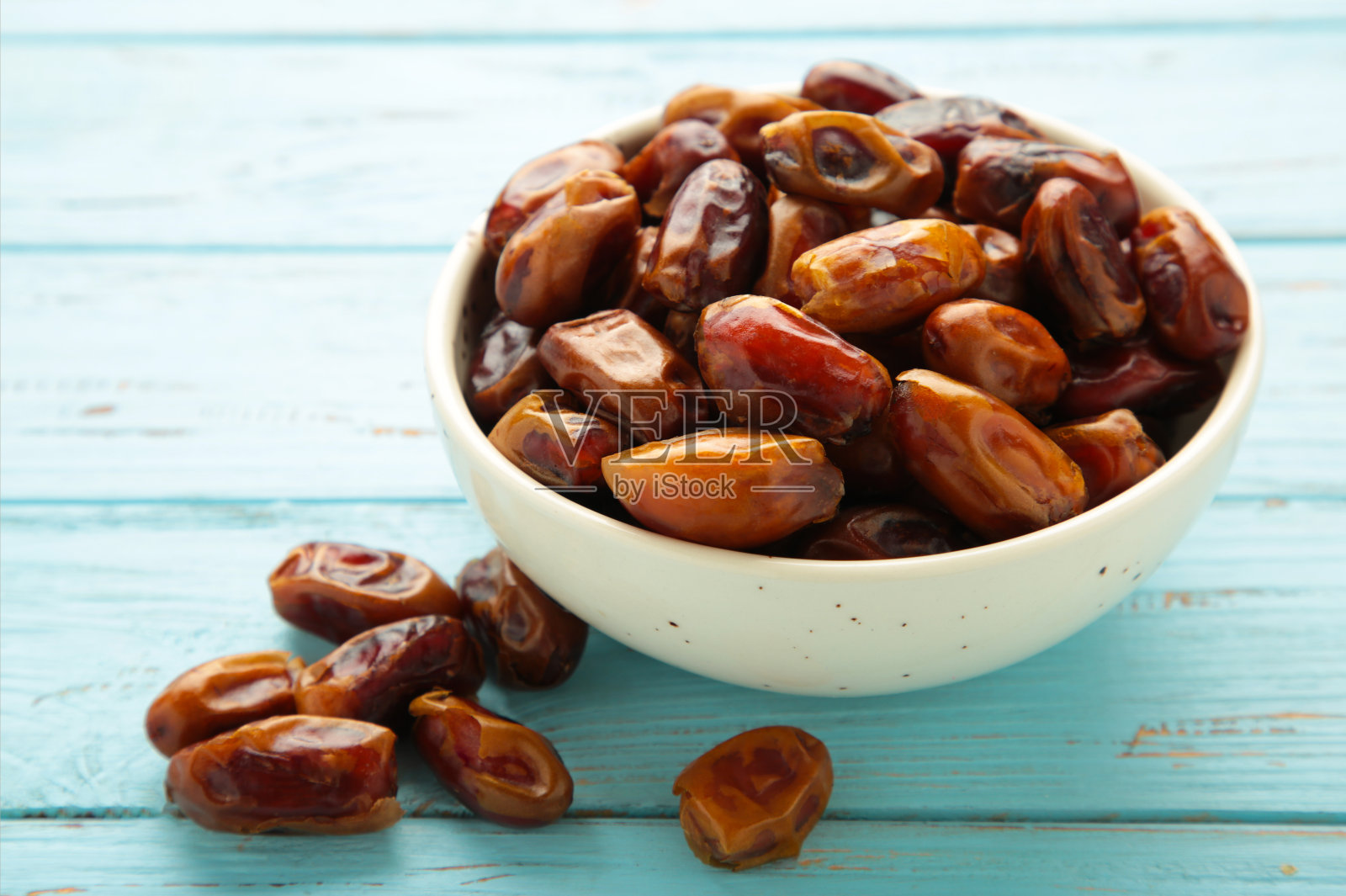 新鲜的枣在蓝色背景的白色碗。近距离照片摄影图片