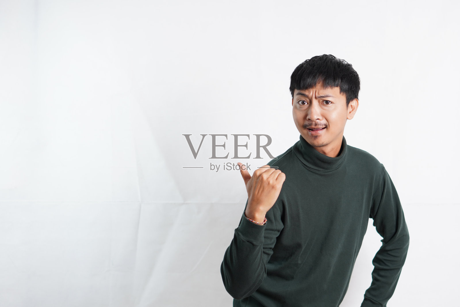 年轻人穿着休闲的绿色t恤，看着镜头，用手和手指指着旁边。照片摄影图片