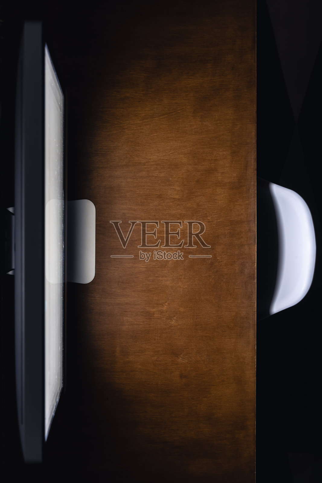 在黑暗的房间里，木桌上的电脑显示器，俯视图。照片摄影图片