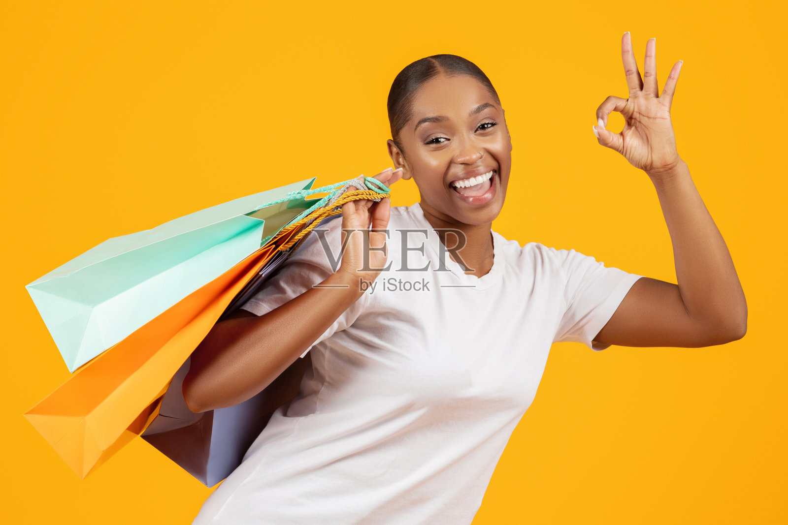 带着购物袋的兴奋黑人女性在摄影棚做着“没问题”的手势照片摄影图片