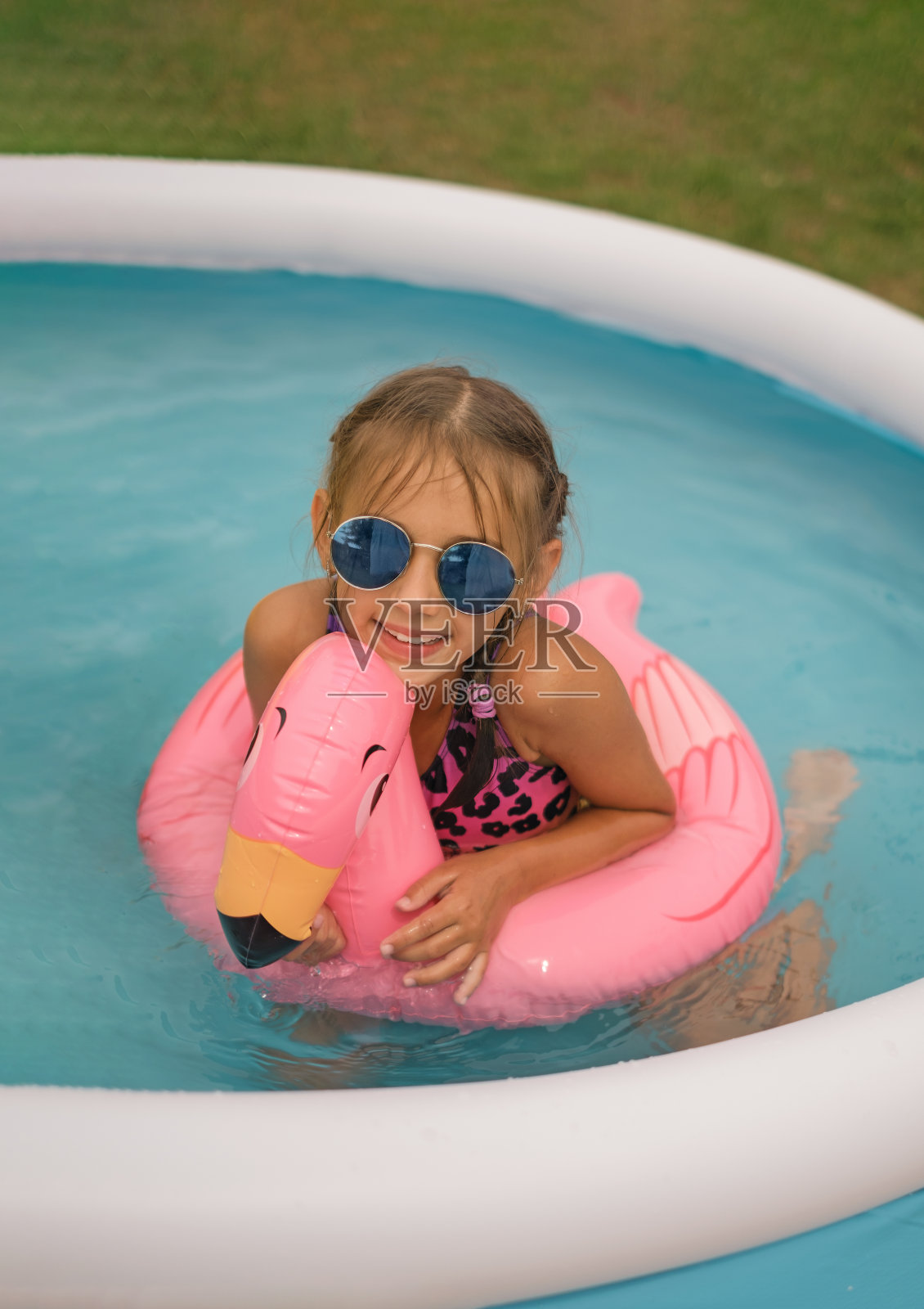 一个孩子在一个充气的迷你游泳池里游泳，游泳池里有一个火烈鸟形状的粉红色圆圈。照片摄影图片