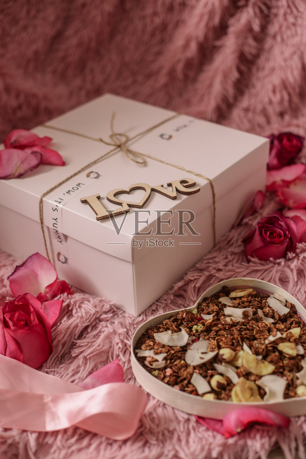 粉红色的桌子上放着一个心形的盒子，里面有坚果、巧克力和香蕉味的格兰诺拉麦片照片摄影图片