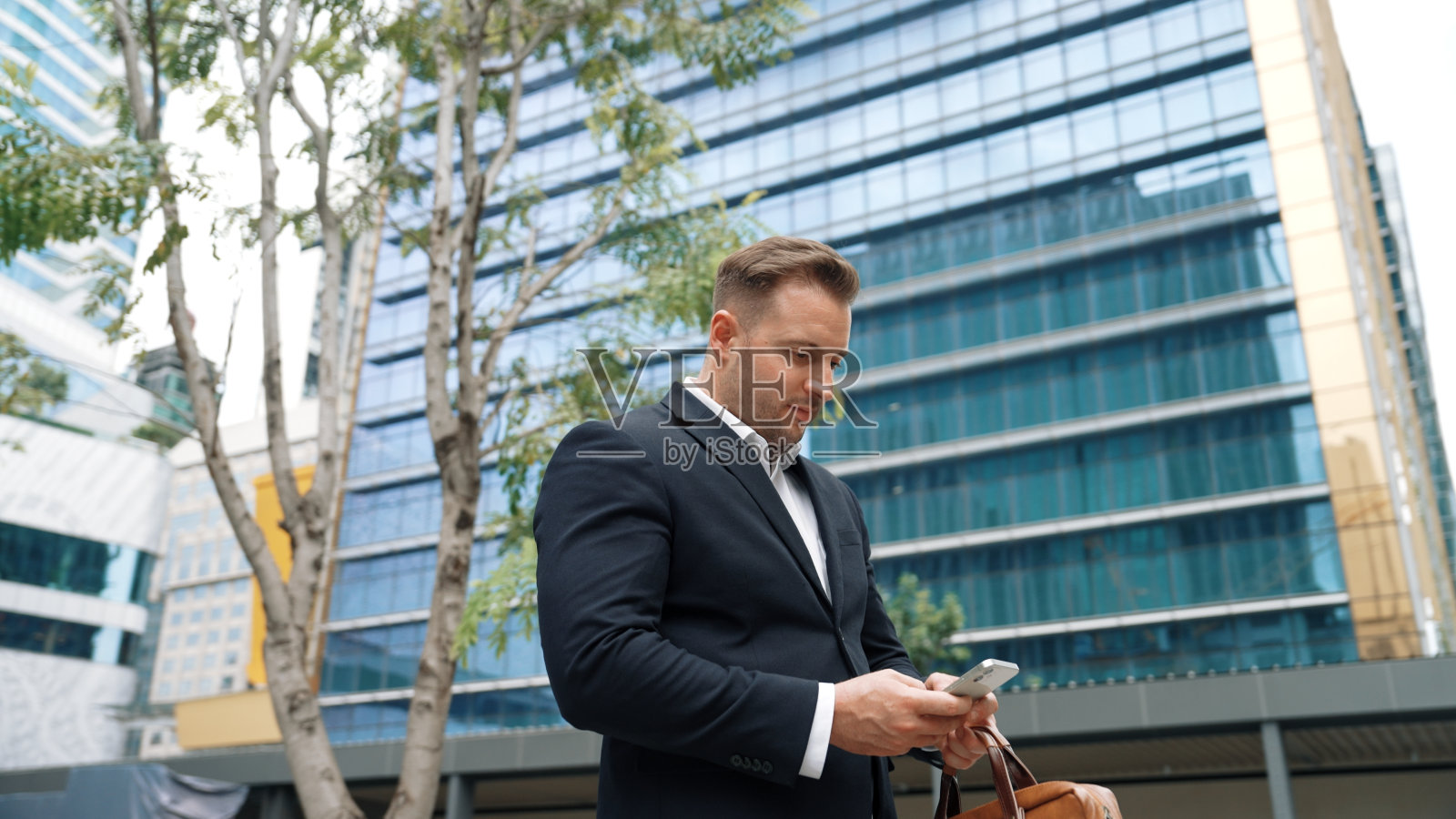 商人一边看手机一边打电话给城市智慧队。彬彬有礼的。照片摄影图片