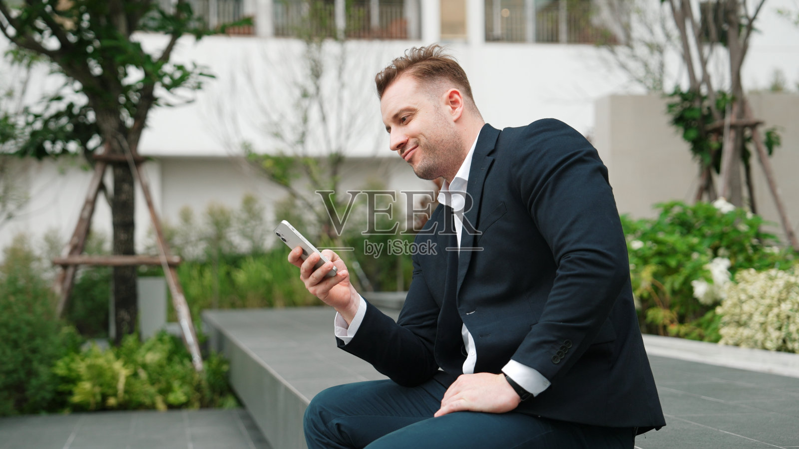 快乐的商务人士坐在绿城里看智能手机。彬彬有礼的。照片摄影图片