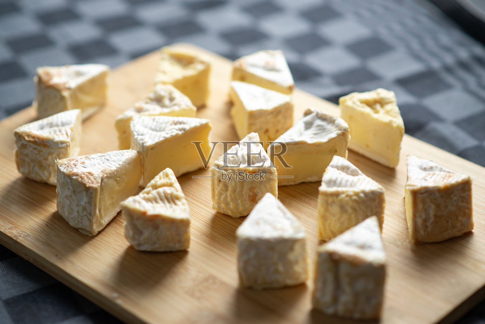 在深色背景下，在砧板上切成三角形的卡曼贝尔奶酪照片摄影图片