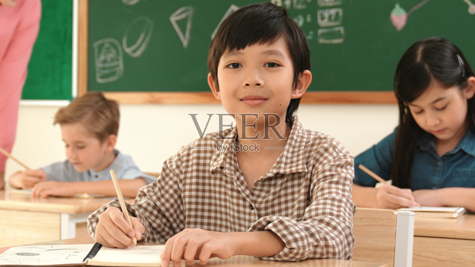 当学生在答题卡上写答案时，男孩对着镜头微笑。教育学。照片摄影图片