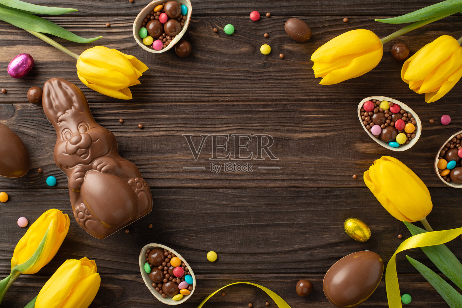 复活节礼物灵感。俯视图:巧克力蛋被打开，里面有糖果，巧克力兔子，郁金香放在木桌上，留下空白的地方放文字或广告照片摄影图片