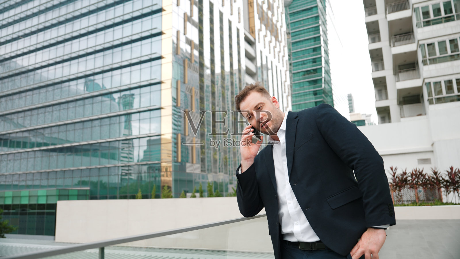 商人站在摩天大楼前用电话与团队通话。彬彬有礼的。照片摄影图片