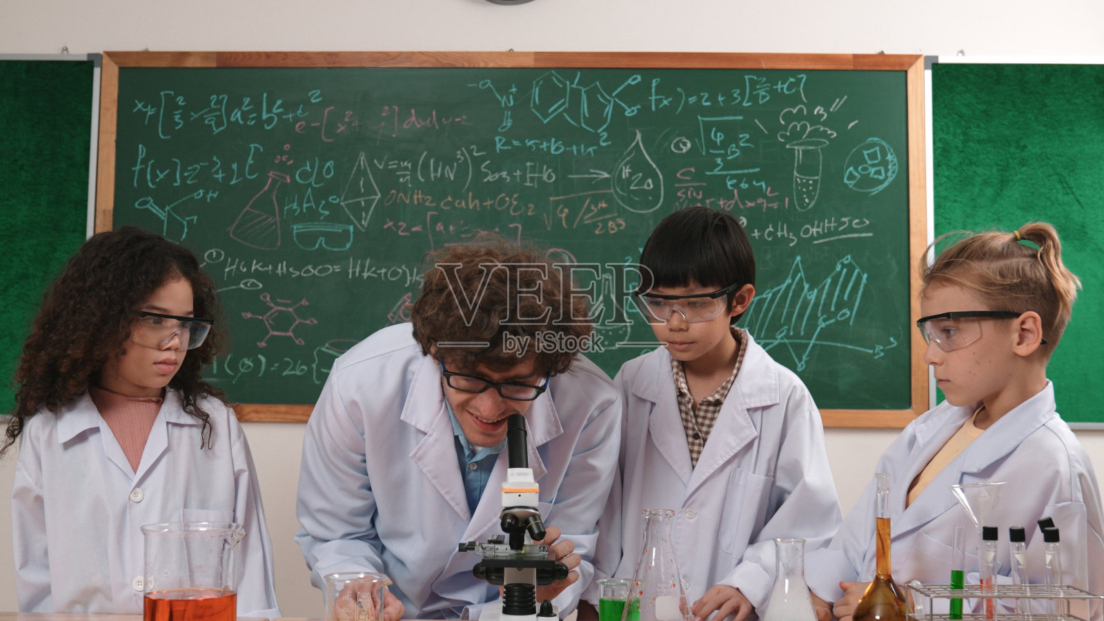 有魅力的老师站在黑板前看显微镜。教育学。照片摄影图片