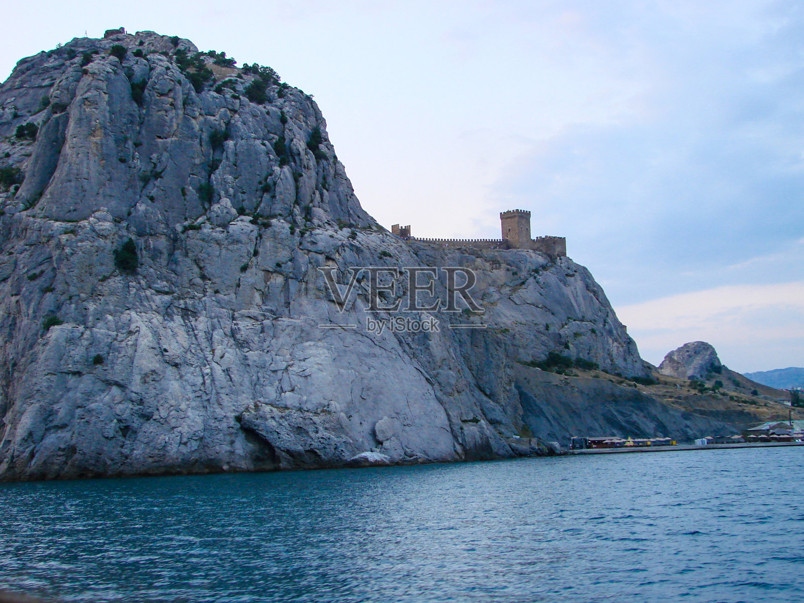在平静的水面上矗立着一块带有明显土壤纹理的岩石，边缘有一座罗马式的堡垒。照片摄影图片