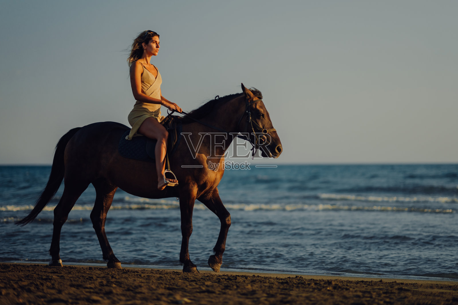 一个穿着裙子的年轻女子在海滩上骑马的侧视图。照片摄影图片
