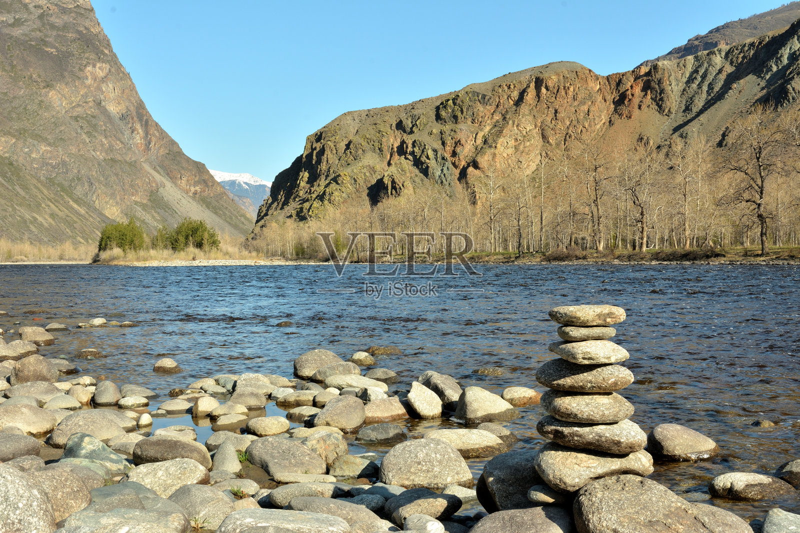 在一个阳光明媚的春日，美丽的山间河流的卵石河岸上的一个低矮的石堆。照片摄影图片