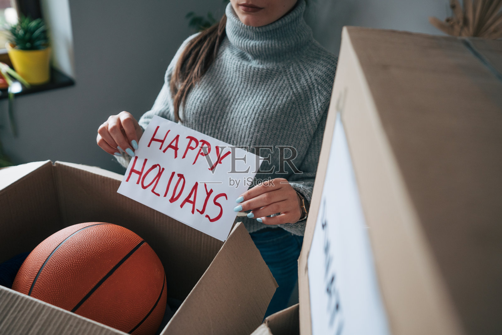 小女孩手里拿着一张写着节日快乐的纸，一边为慈善机构打包东西照片摄影图片