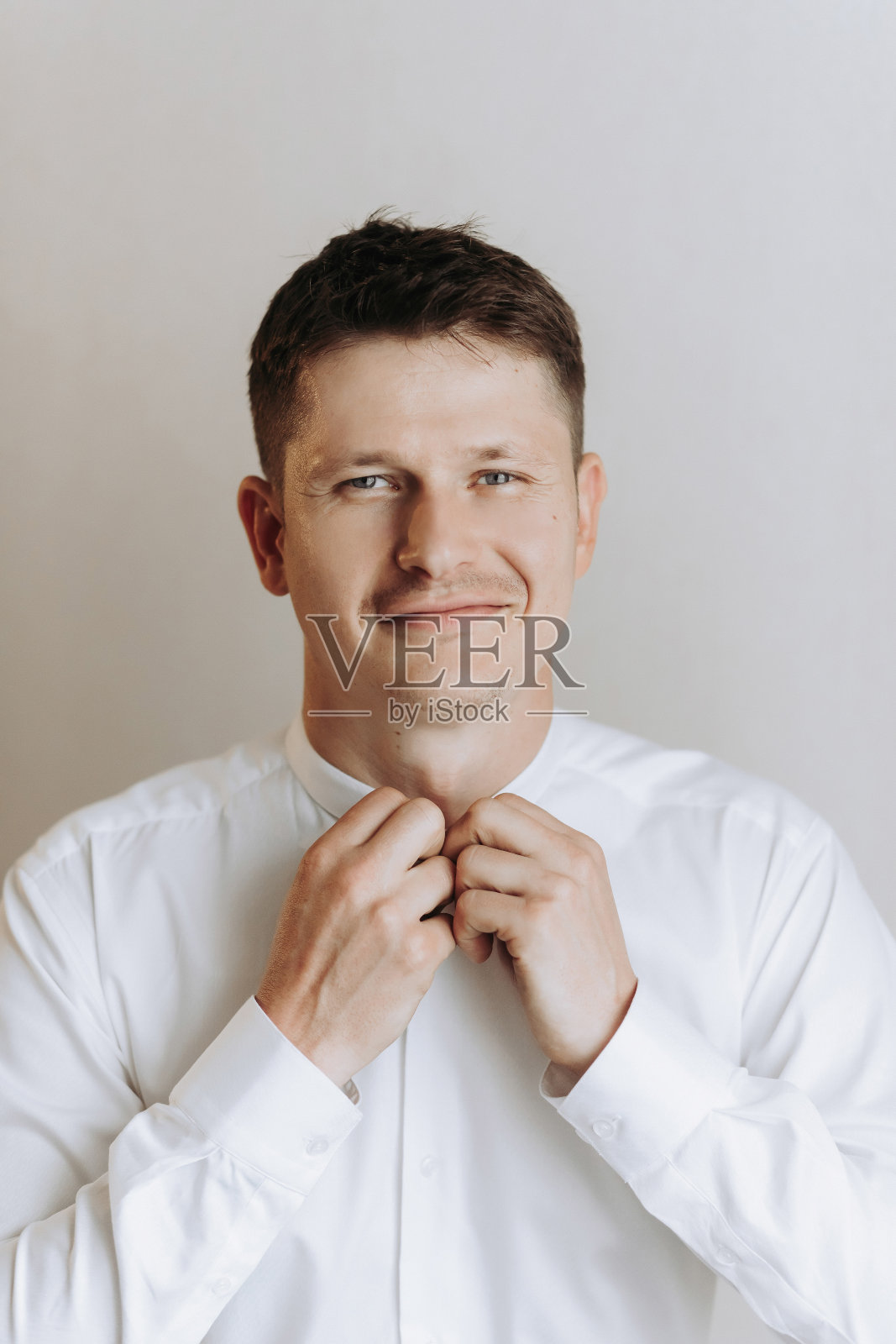 一位时髦的新郎正在为婚礼做准备。新郎的早晨。一位商人正在扣白衬衫的扣子。婚礼前的早晨，新郎正在做准备照片摄影图片