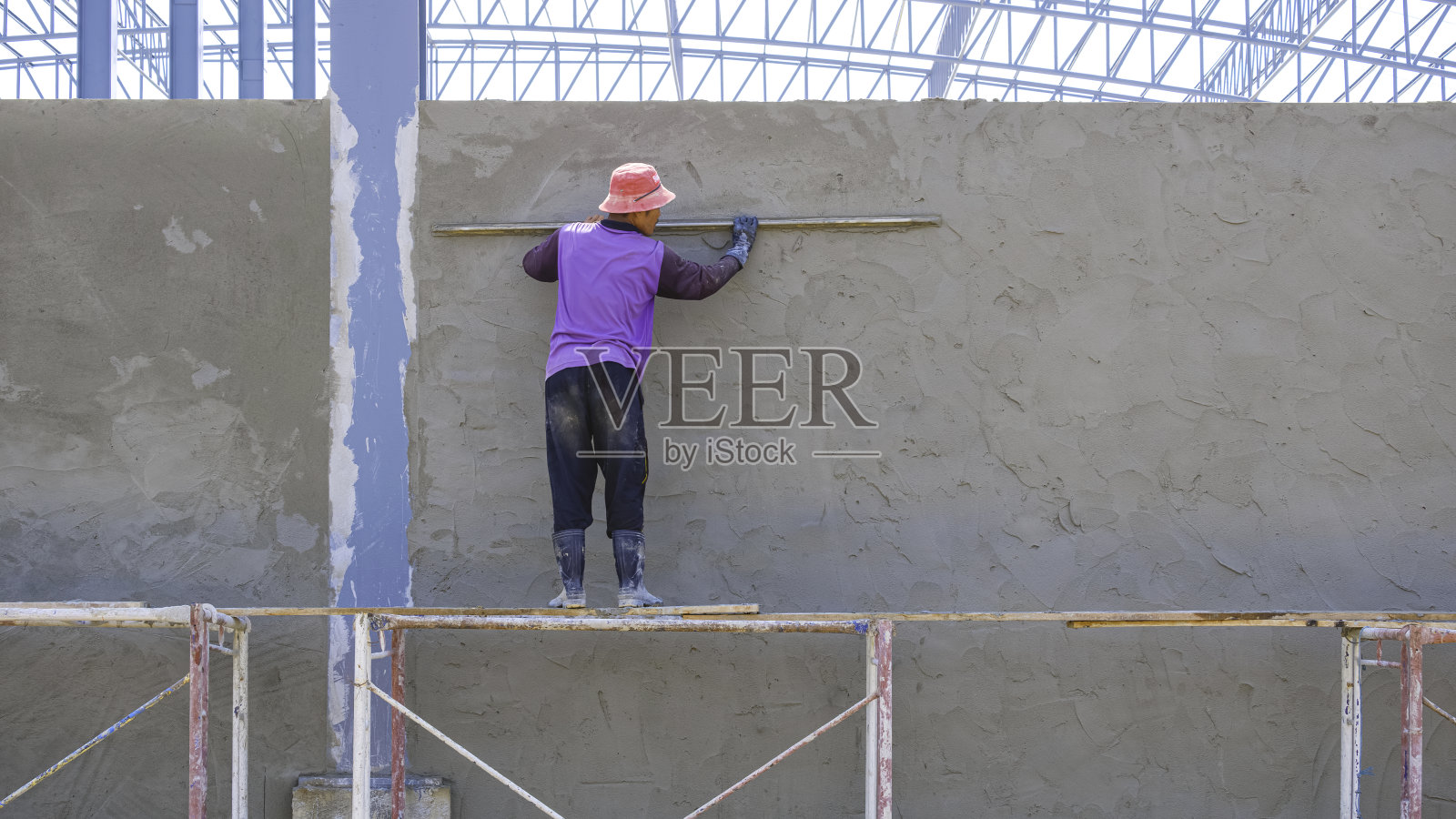 亚洲脚手架抹灰工是在施工现场用长抹刀在工业厂房墙面上抹灰水泥照片摄影图片