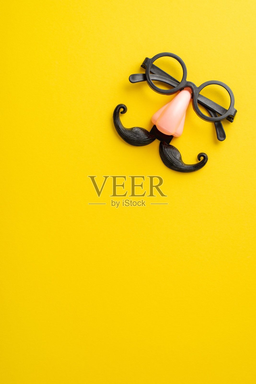 进入愚人节的精神:垂直俯视图滑稽的眼镜与假胡子和鼻子，展示在一个明亮的黄色帆布上，与您的个性化文字或广告的空间照片摄影图片