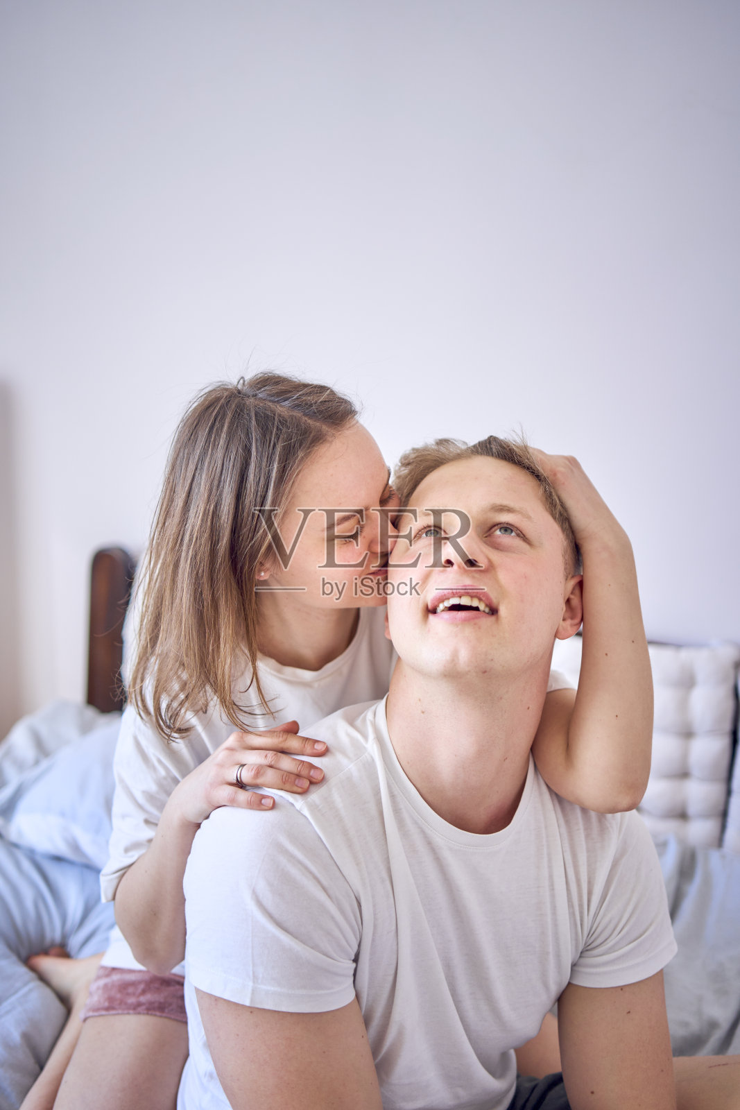 一对年轻夫妇在床上，女人玩耍，咬男孩的耳朵照片摄影图片