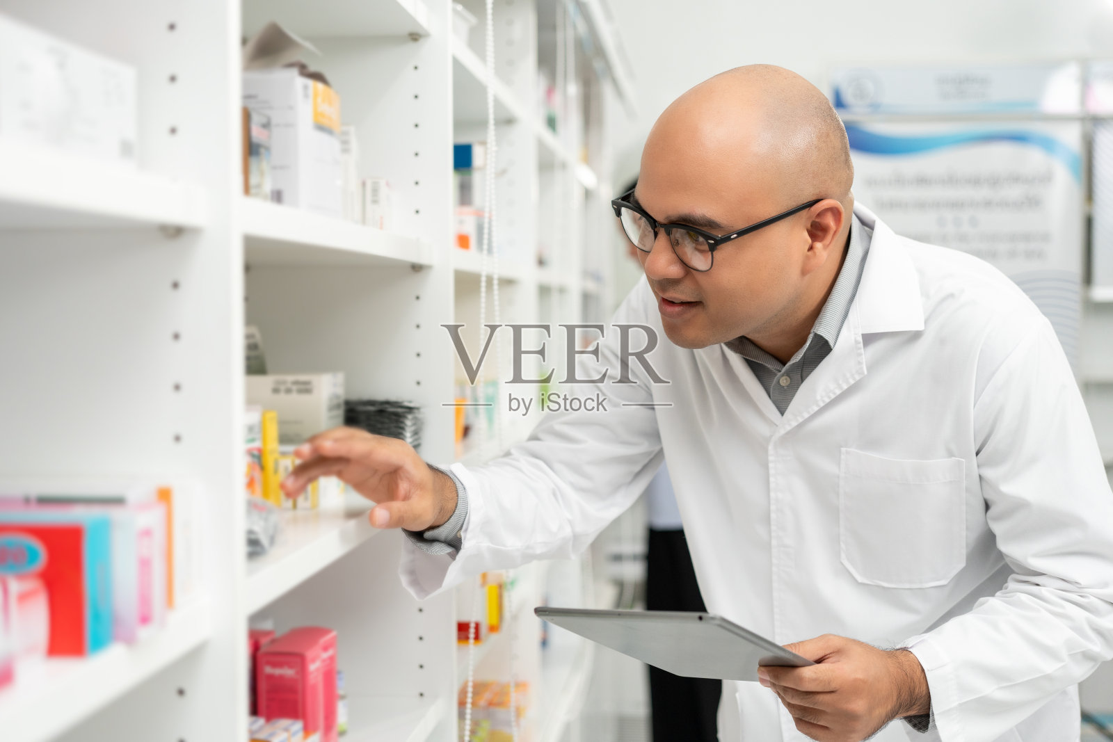专业的亚洲男药剂师检查药房药品的库存安排。穿着制服的男药剂师站在药品货架旁给顾客开处方照片摄影图片