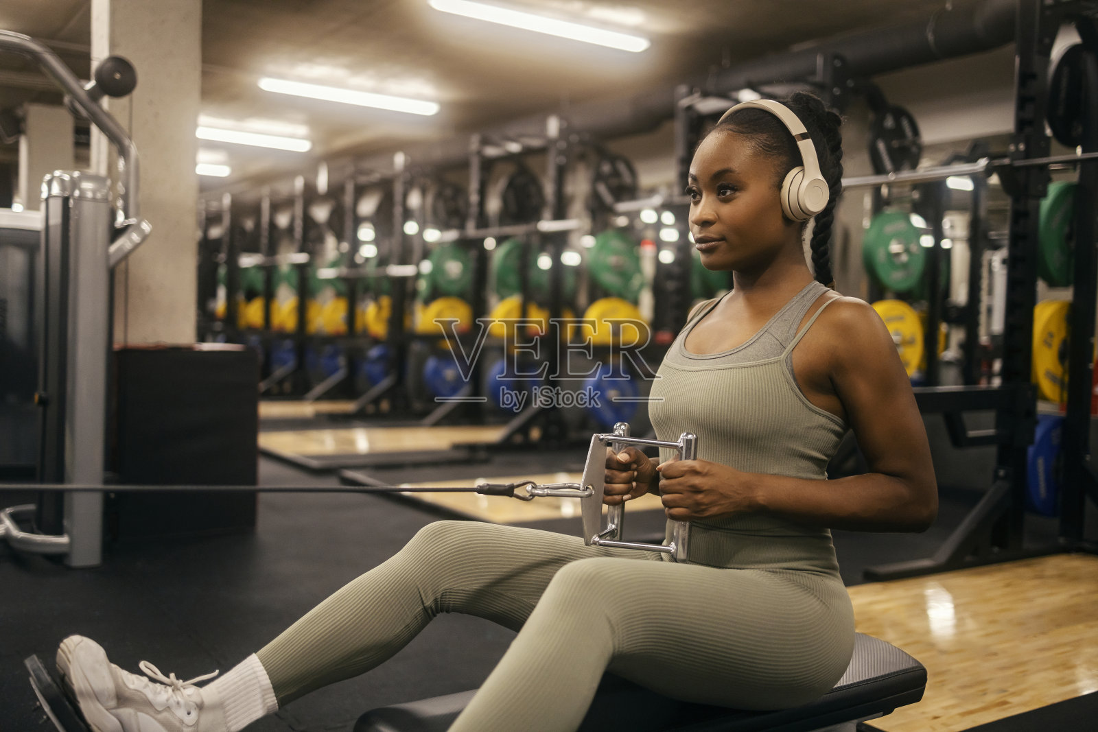一个年轻有力的非裔美国女运动员戴着耳机在有线电视上锻炼背部。照片摄影图片