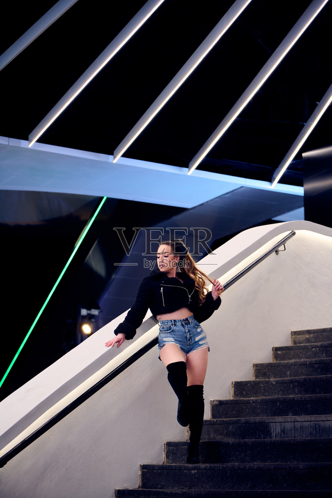 漂亮的金发女孩穿着牛仔短裤和黑色夹克在街上摆姿势照片摄影图片