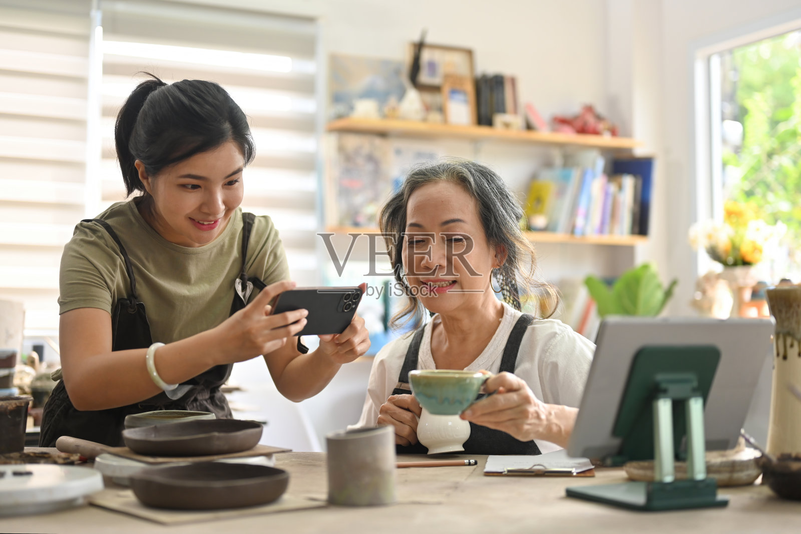 两名陶瓷店主使用智能手机拍摄陶瓷产品的照片，用于在线市场和销售以及电子商务。照片摄影图片