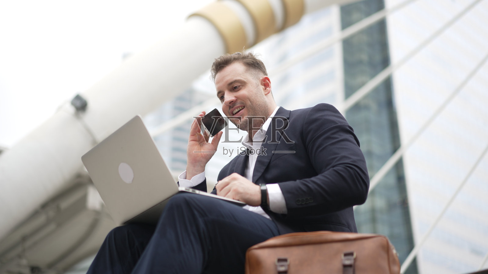 一个白人商人坐在楼梯上使用笔记本电脑和手机。彬彬有礼的。照片摄影图片