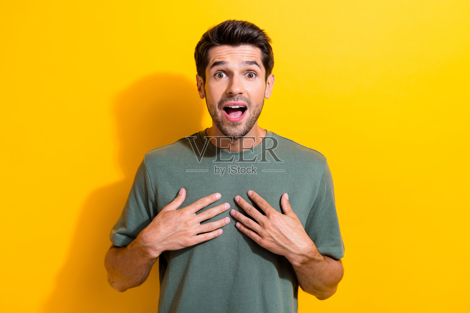 无话可说的家伙的肖像，胡茬手放在胸前，惊讶地盯着难以置信的胜利孤立在黄色背景照片摄影图片