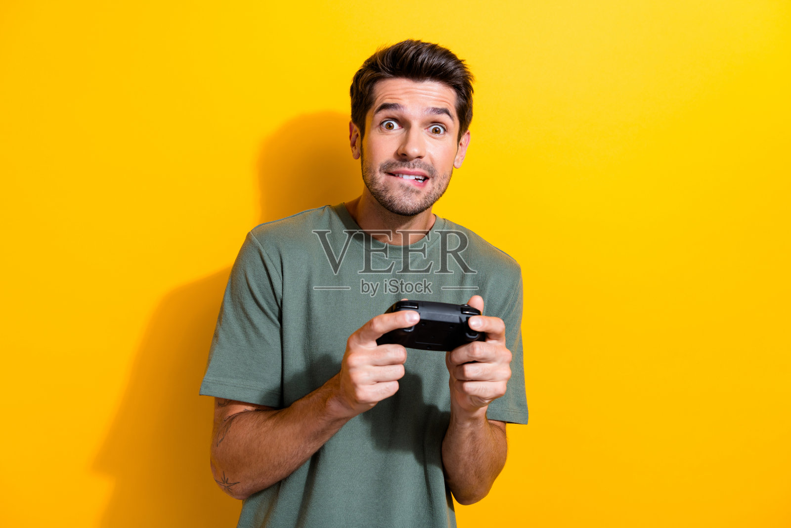 肖像集中印象深刻的家伙与胡茬穿着时尚的t恤拿着游戏机操纵杆孤立的黄色背景照片摄影图片