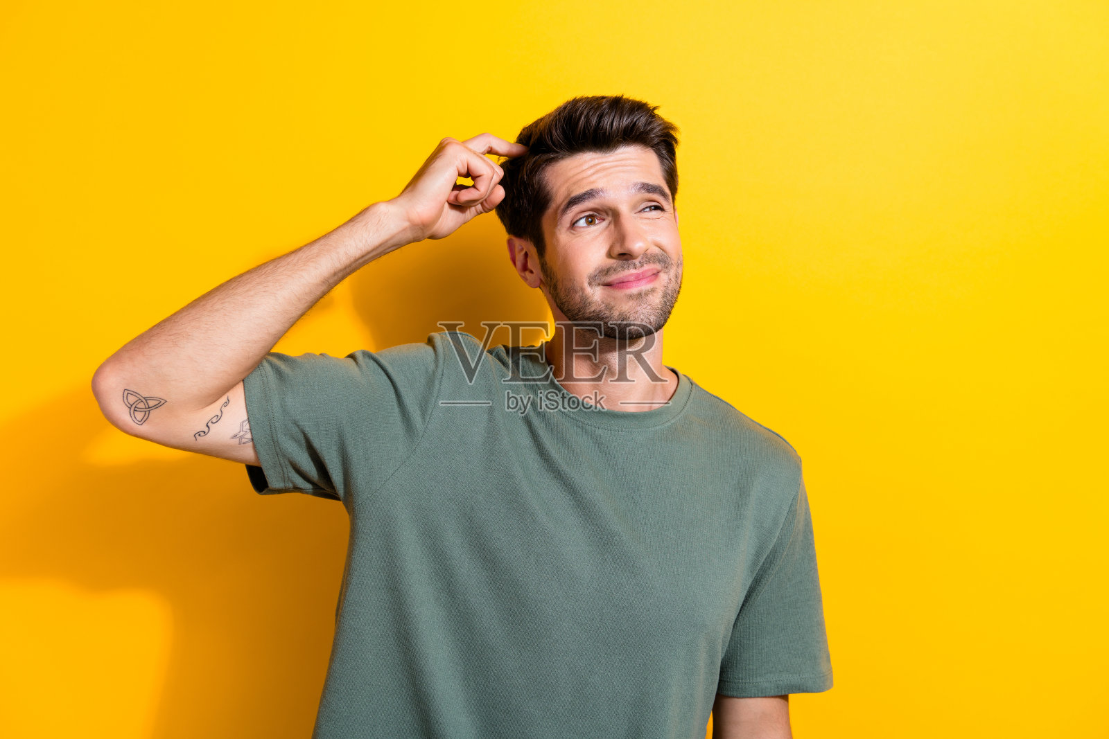 健忘的家伙的肖像，留着胡茬，穿着时尚的t恤，抓挠头，看黄色背景上孤立的空白空间照片摄影图片