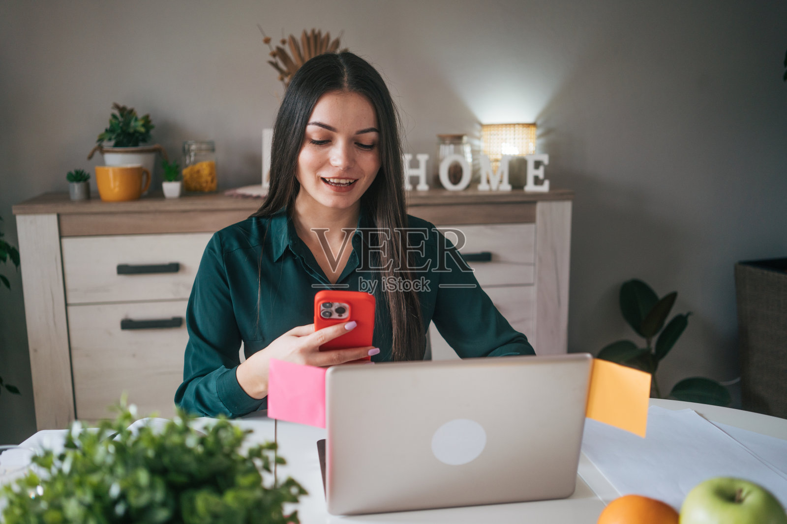年轻微笑的女人坐在家里使用笔记本电脑。照片摄影图片