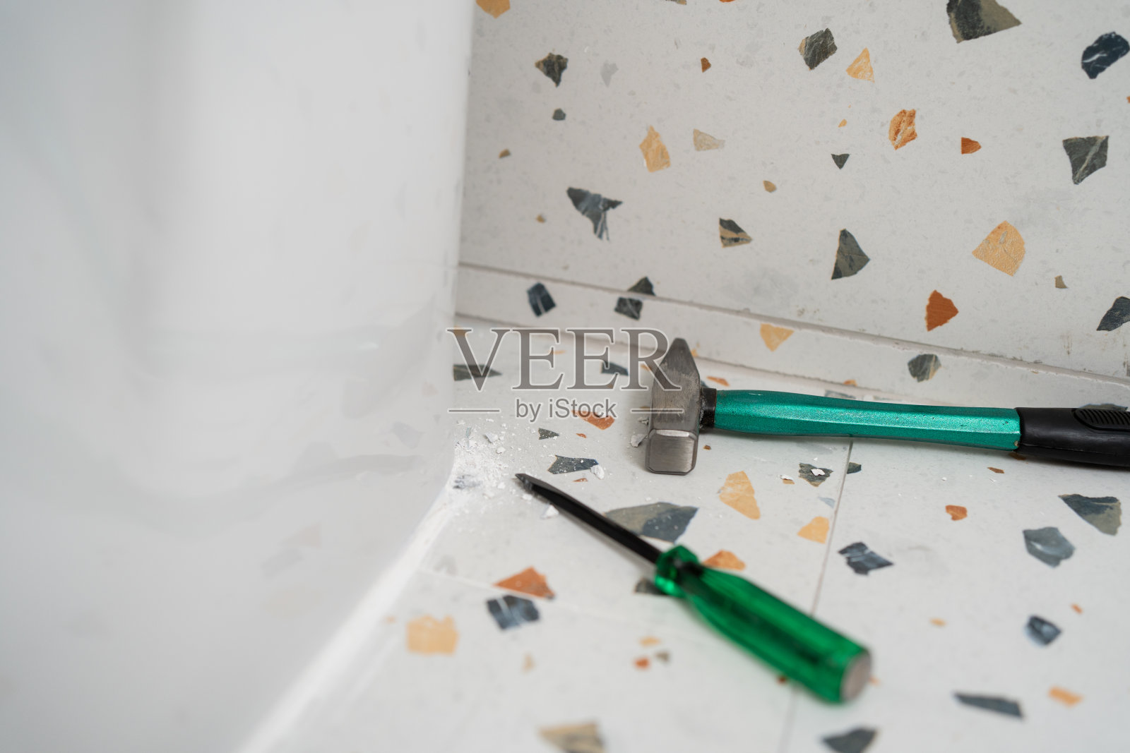 用绿色锤子和绿色螺丝刀冲洗马桶底座上的白色水泥。更换或修理照片摄影图片