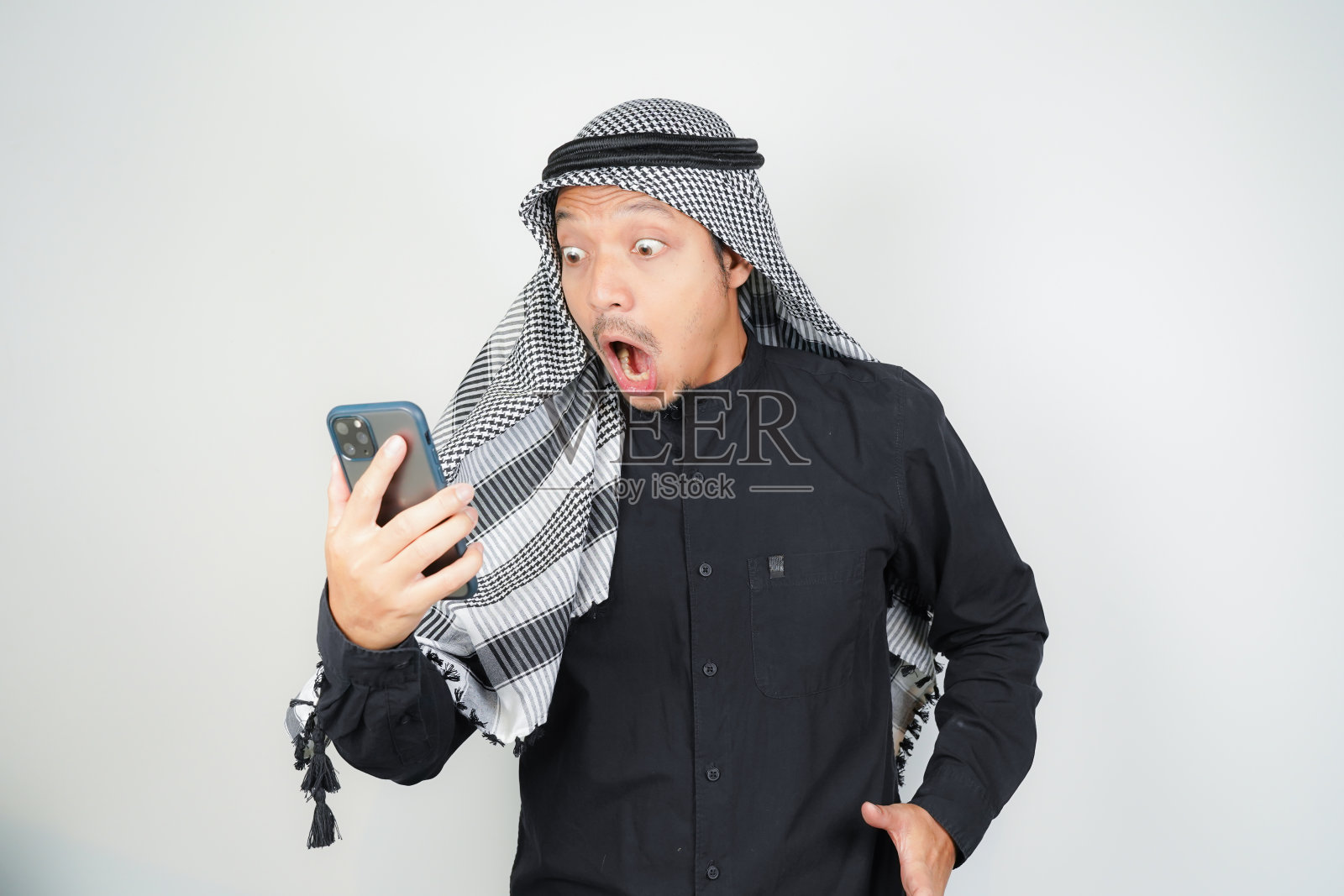 现在，一个戴着阿拉伯头巾的亚洲穆斯林男子的脸震惊了他在孤立的智能手机中看到的一切照片摄影图片