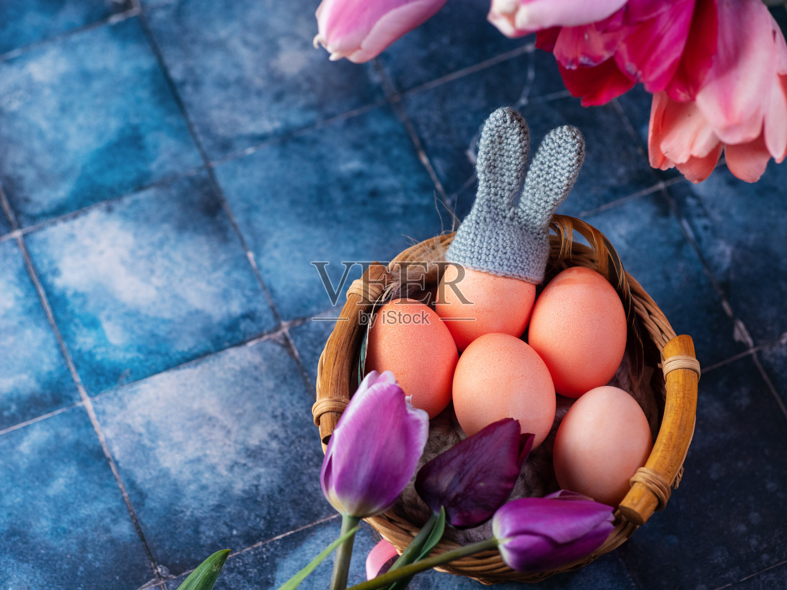 复活节快乐的横幅上有蓝色背景的篮子里的鸡蛋和五颜六色的郁金香。俯视图复制空间照片摄影图片