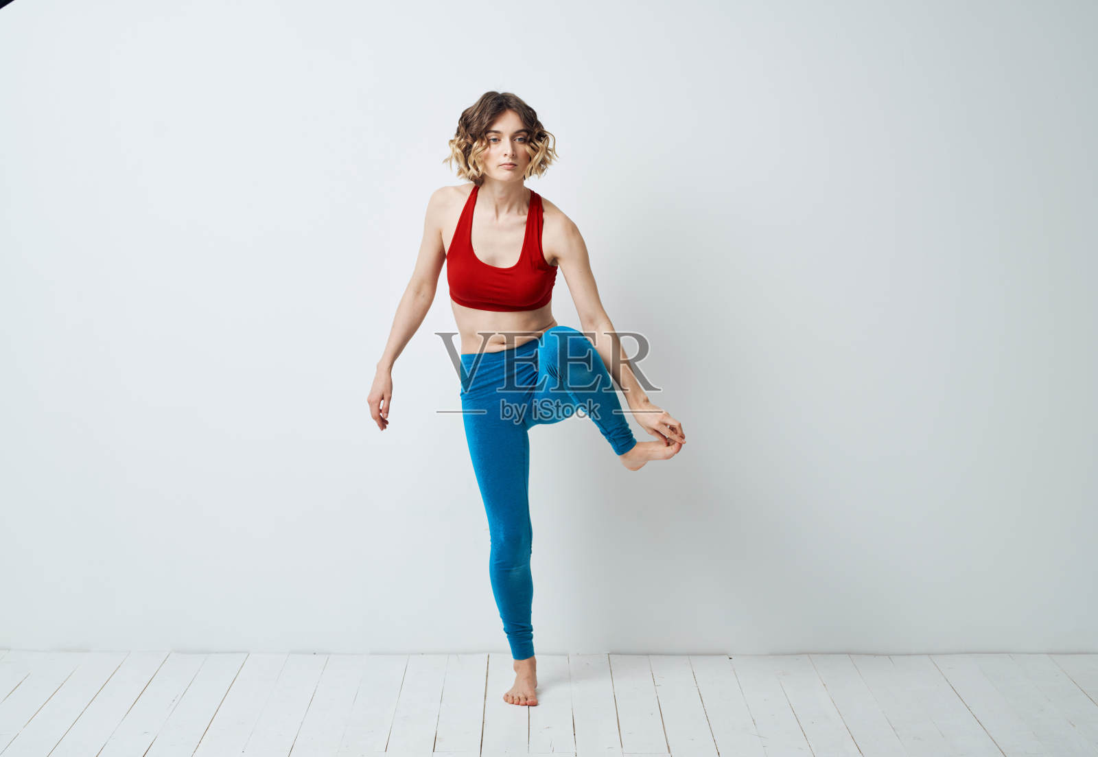 穿着蓝色打底裤的女人在室内光线充足的地板上做运动照片摄影图片