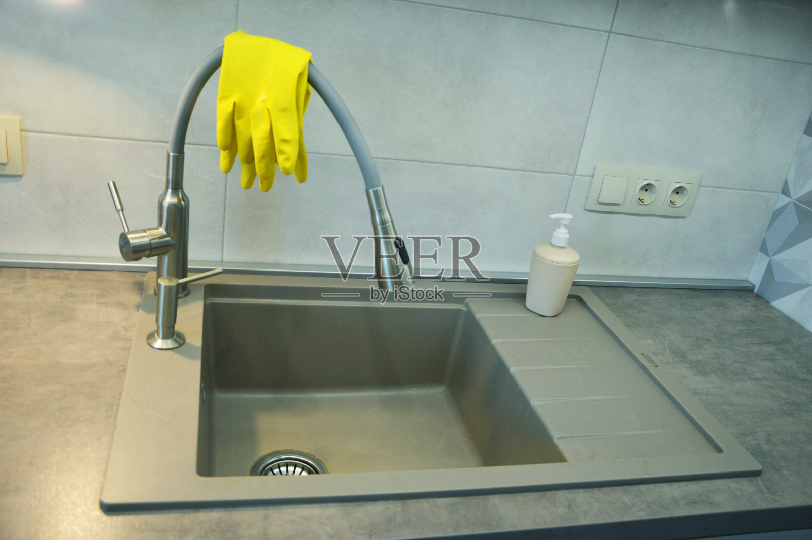 厨房水槽有可弯曲的水龙头，没有盘子。水龙头上有黄色的清洁手套。照片摄影图片