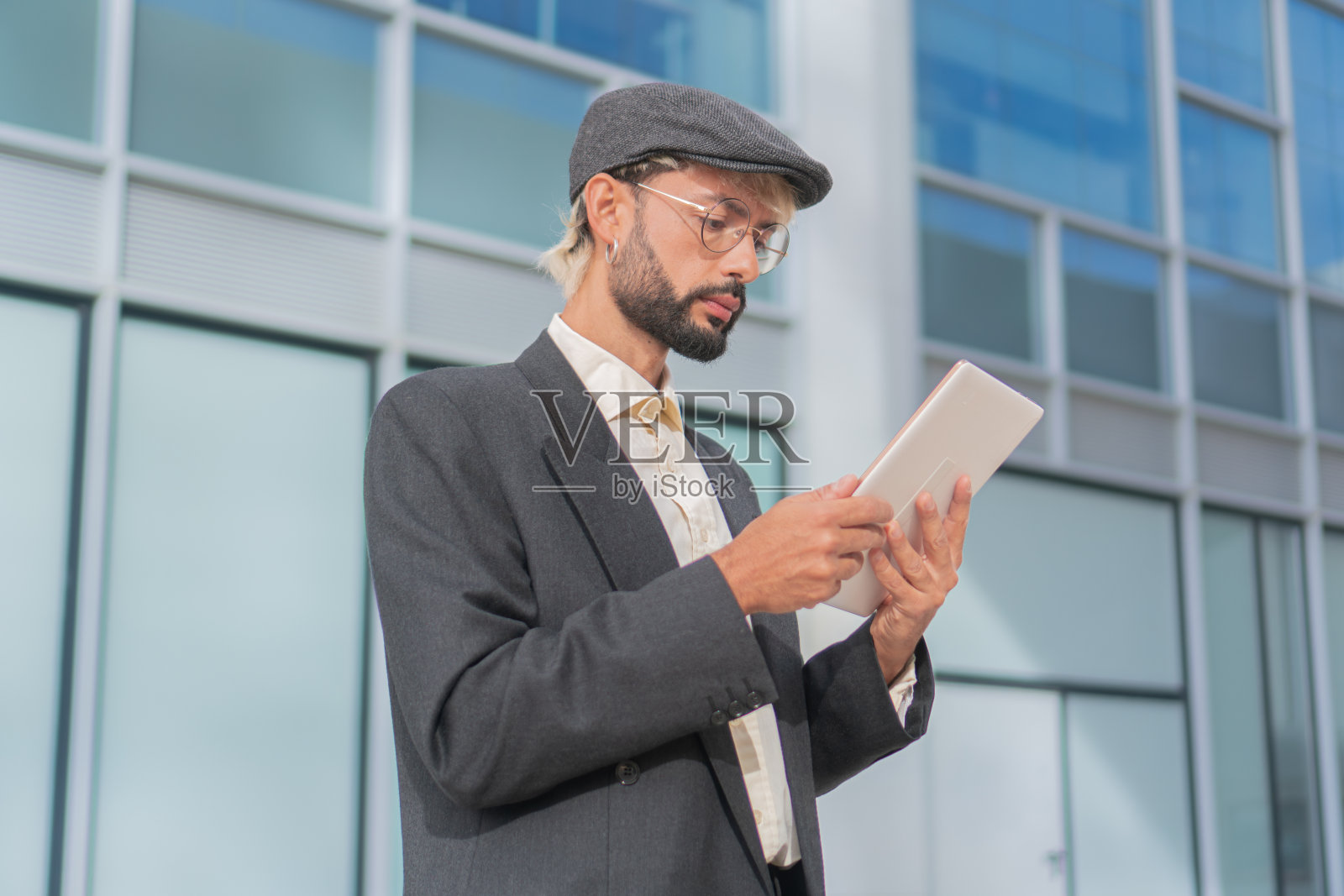 一位年轻的成年商人在公司大楼外摆弄他的平板电脑。自信的企业家穿着西装站在网上使用设备照片摄影图片