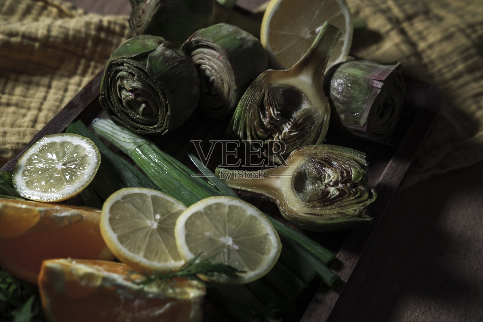 新鲜的洋蓟花蕾配上柠檬、橘子、葱、香草，放在木板上，黄台布厨房纺织，蔬菜准备烹饪照片摄影图片