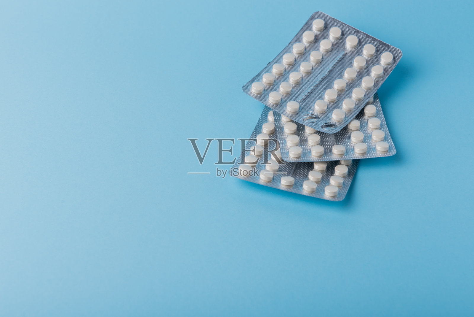 蓝色桌子上的许多白色胶囊片或药片的医学背景。关闭了。保健药学和医学概念与复制空间。照片摄影图片