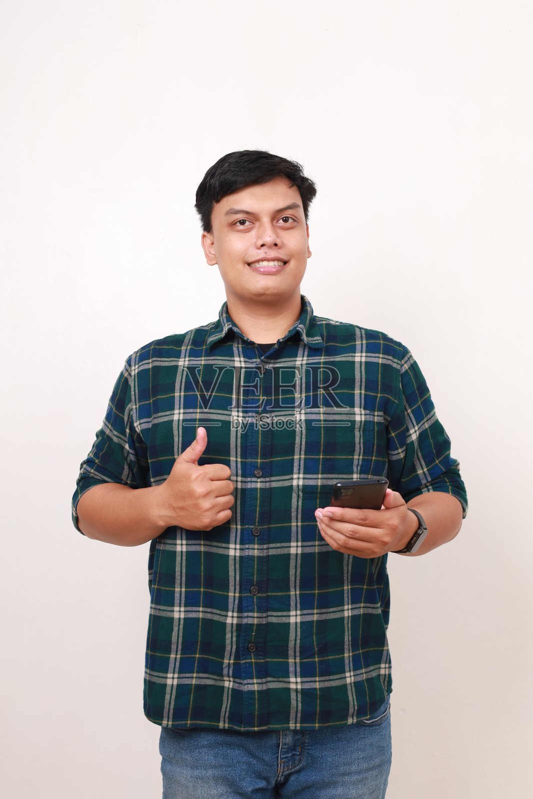 年轻的亚洲男子的肖像拿着手机，同时竖起大拇指照片摄影图片